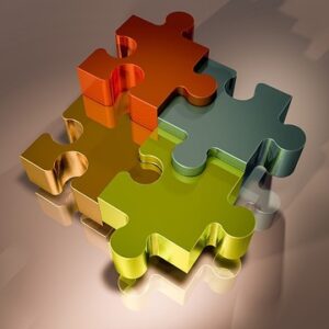 Fyra tredimensionella pusselbitar i metallic-glänsande färger (guld, orange, olivgrön och blågrön) ligger i mitten av en nougatfärgad bakgrund. Bilden används som produktbild till jobbpaket-premium för arbetsgivare.