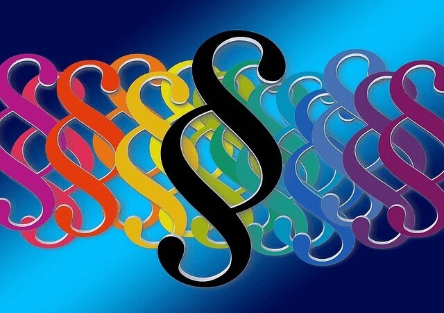 En bild med en rad färgglada paragraftecken som går från rött till lila från vänster till höger, med ett svart paragraftecken i centrum. Bakgrunden är mörkblå som tonar diagonalt till ljusare blå. Bilden används i ett inlägg om arbetsrätt och arbetsmiljö.