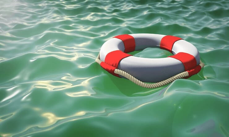 Vit livboj med röda band som flyter på en grönaktig vattenyta med krusningar och ljusblänk. Symboliserar stöd och trygghet i samband med ett inlägg som uppmuntrar till att bli stödperson.