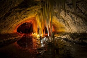 Bild på en med varmt sken upplyst grotta där det finns fantastiska stalaktiter som hänger från taket. Bilden bidrar till namnsdags-inläggets visuella design.