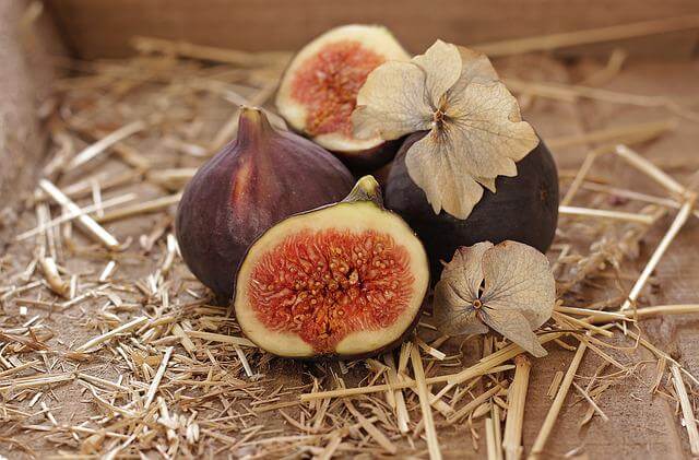 Stilleben av hela och delade fikon samt torra, papperslika foderblad från physalis på en bädd av kartong och halm. Bilden bidrar till sidans visuella design.